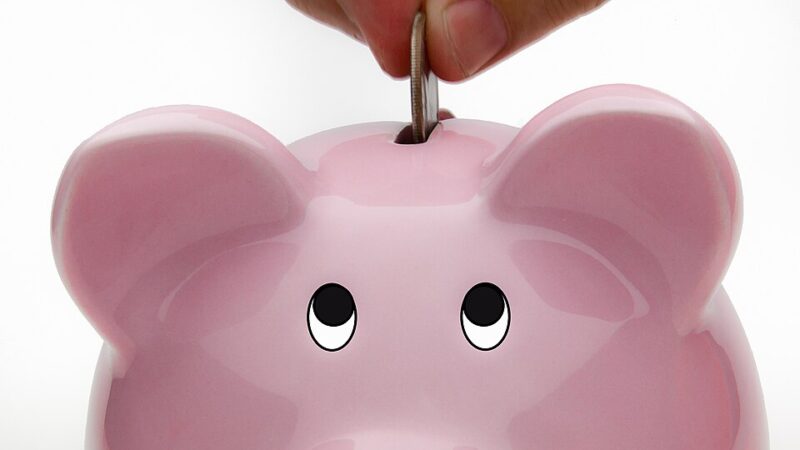 Hand depositing a coin into a pink piggy bank