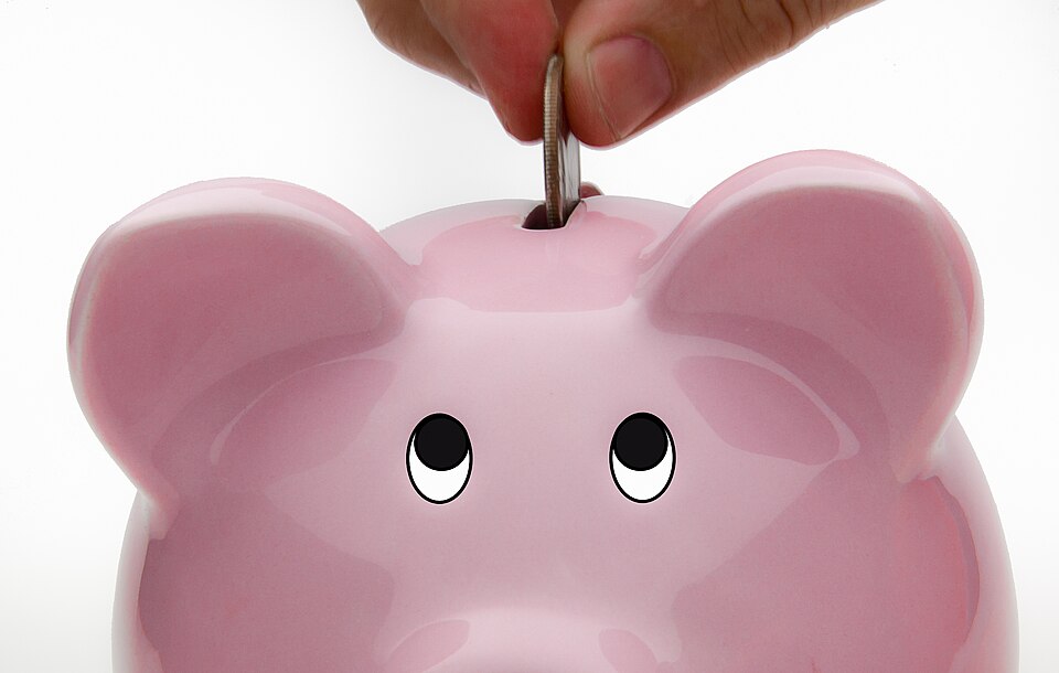 Hand depositing a coin into a pink piggy bank